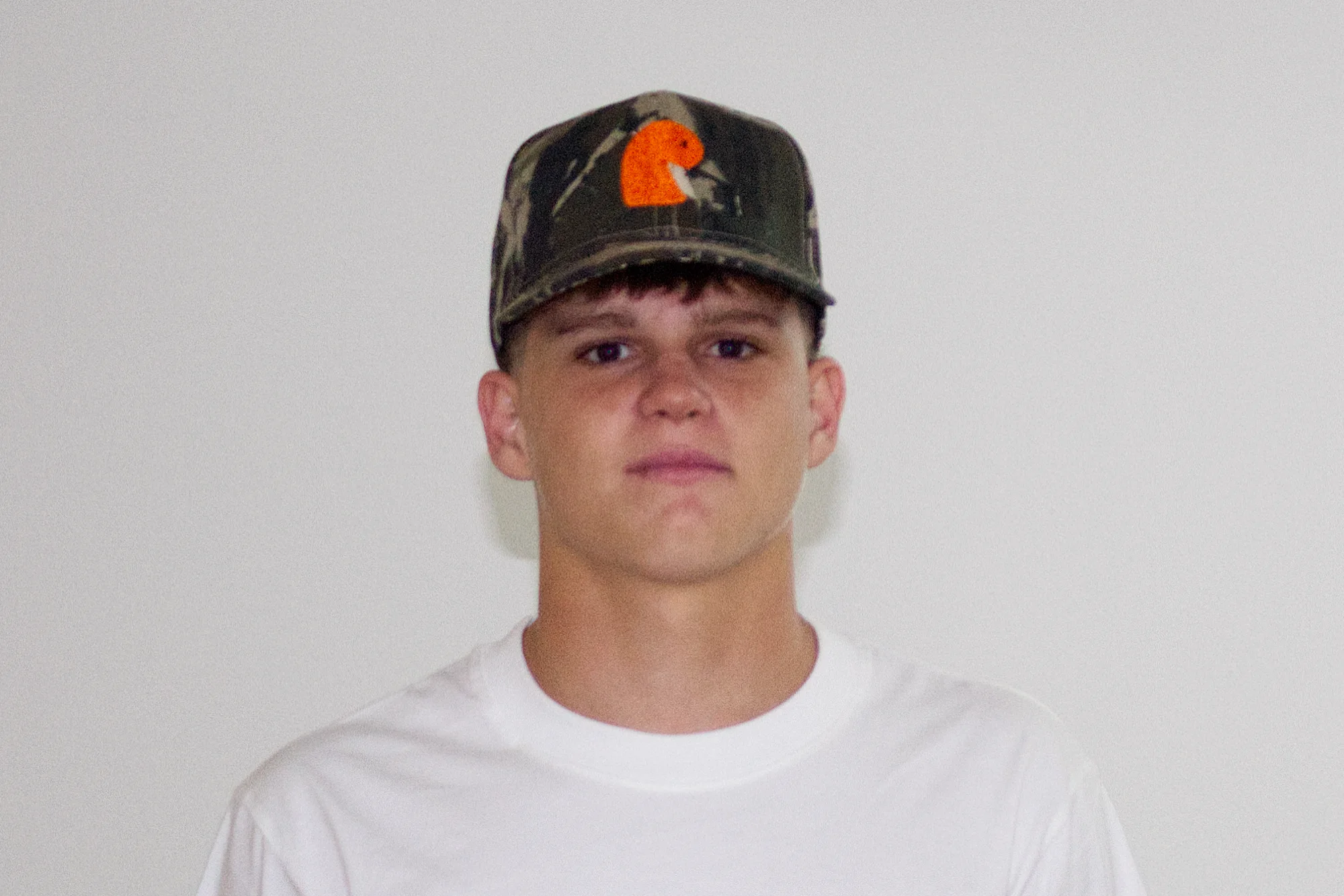 EMVŸ camo cap with the orange embroidered mark, worn front-on