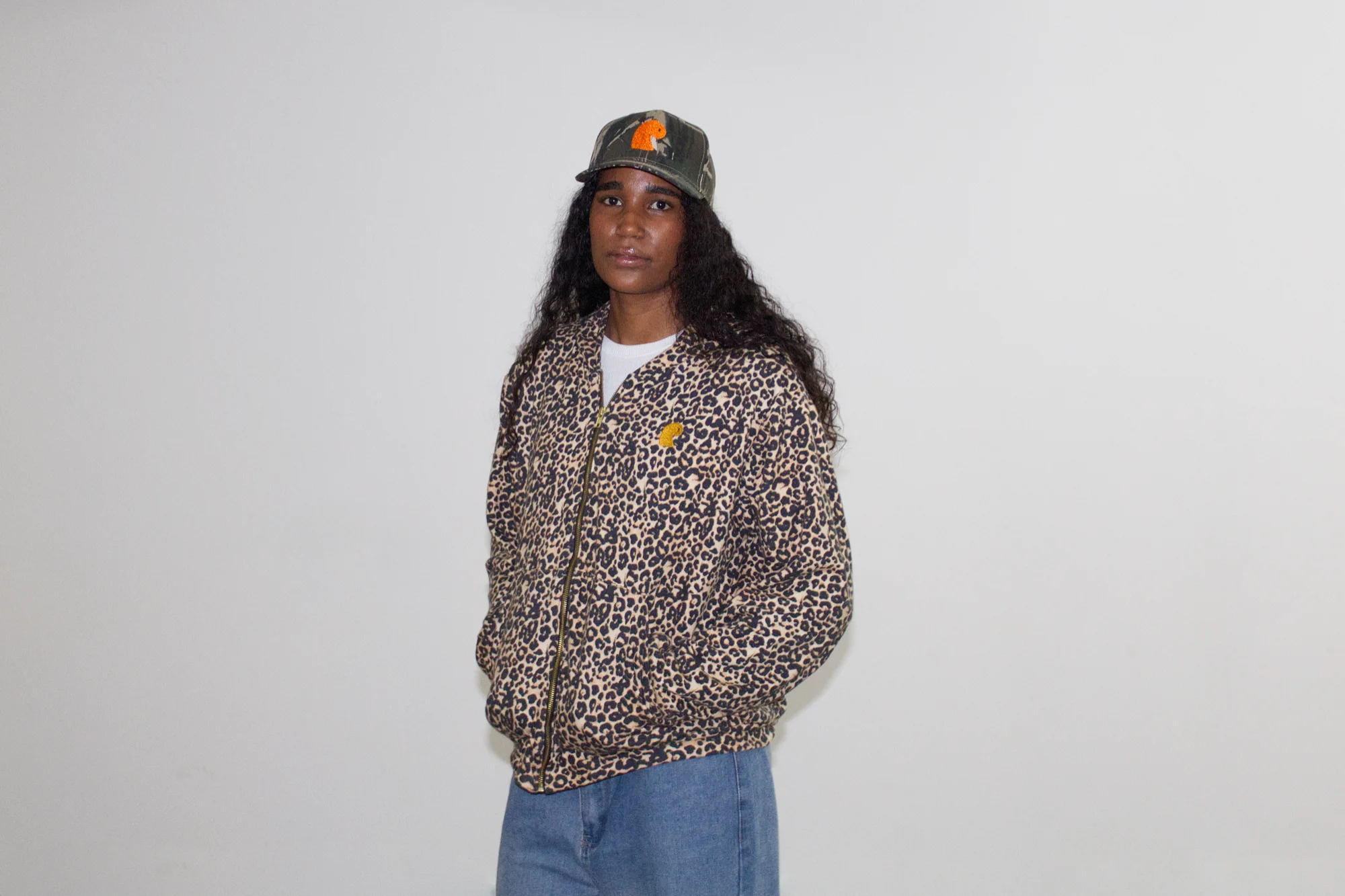 Leopard-print EMVŸ cheater hoodie zipped up, worn front-on with the camo cap