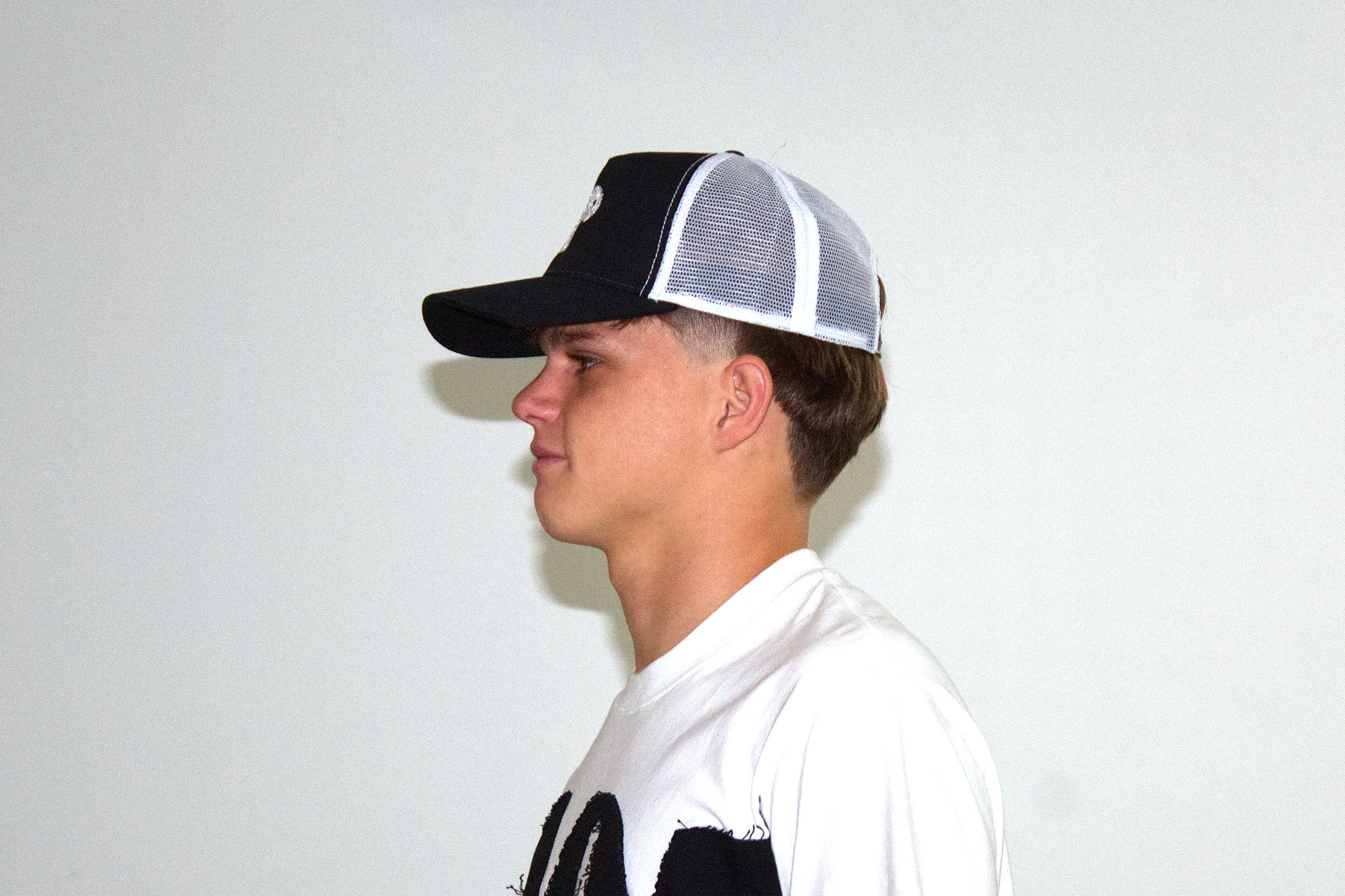 Black trucker cap in profile, showing the white mesh back